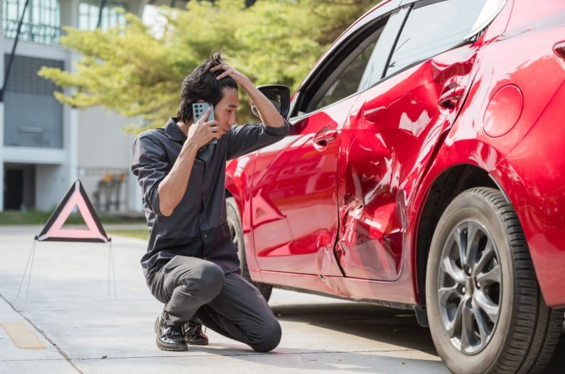 Motorist inspecting a damaged car after a collision, representing a car accident case handled by an Oakland car accident lawyer.