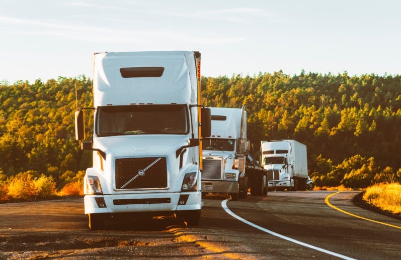 Three semi-trucks on a highway in a rural area, illustrating commercial trucking operations and possible semi-truck accident claims around Oakland, CA.