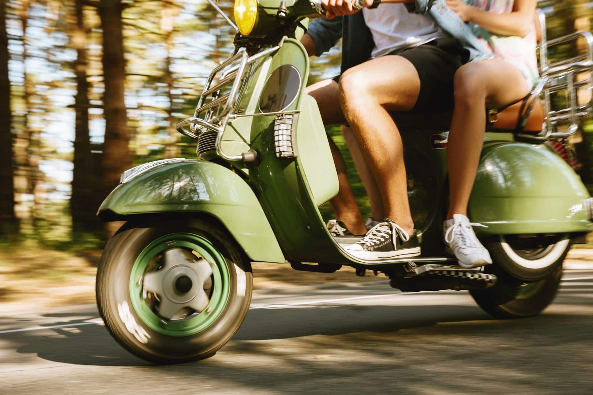 Close-up of a man and a friend riding a green scooter outdoors, a common type of vehicle involved in San Diego scooter accidents.