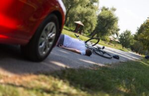 A cyclist lies injured beside a damaged bicycle after a collision with a motor vehicle, highlighting the serious consequences of bicycle accidents and the importance of determining fault under California law.