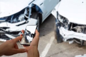Person using a smartphone to photograph damage from a two-vehicle collision, documenting evidence at the scene of a San Diego car accident for an insurance claim or personal injury case.