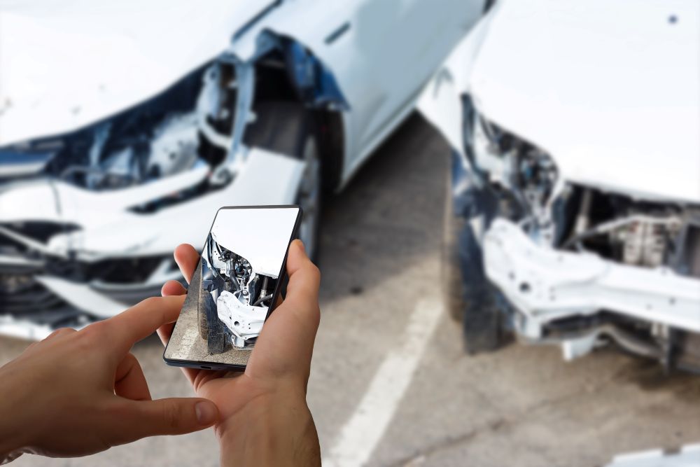 Person using a smartphone to photograph damage from a two-vehicle collision, documenting evidence at the scene of a San Diego car accident for an insurance claim or personal injury case.