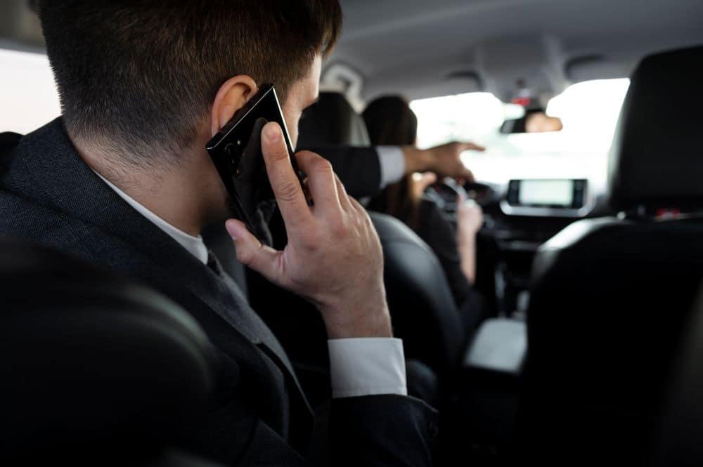 Business professional riding in the back seat of a rideshare vehicle while speaking on a cellphone, with the driver visible ahead, representing Uber transportation, rideshare travel, and potential Uber accident injury claims in San Diego.