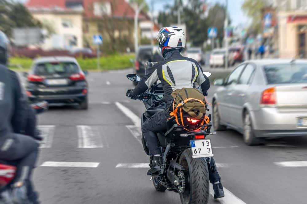 Motorcyclist lane splitting between two cars on a Los Angeles freeway during heavy traffic